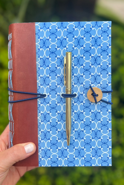 Caderno artesanal azul com lombada vinho, costura aparente, fechamento em elástico e suporte para caneta